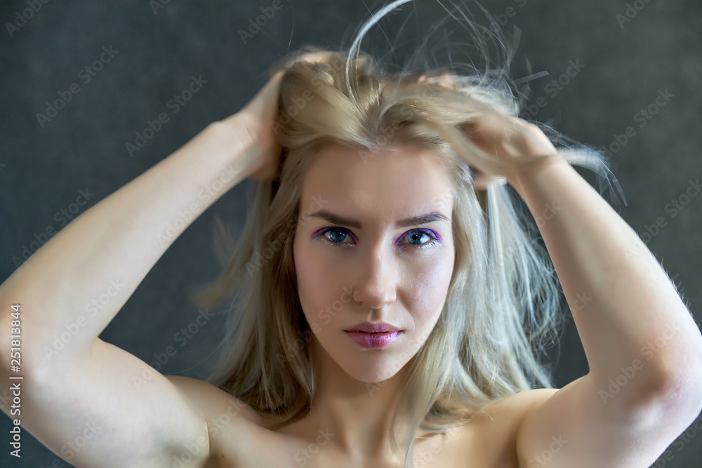 Closeup portrait concept of a beautiful blonde girl on a gray background. Hair develops in different directions.