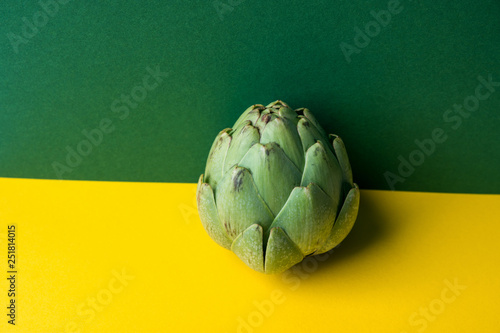 Ripe artichoke on duotone yellow green color combination background. Creative food poster. Minimalist style. Mediterranean Spanish cuisine healthy plant based diet superfoods concept