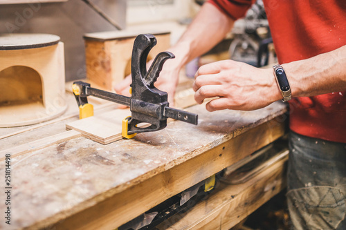 Foto Carpentry workshop - a man fixes wooden parts with glued clamps