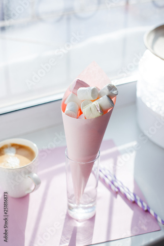 The White cup of hot coffee and sweett marshmallow snack against window with morning light. Morning routine minimal concept photo