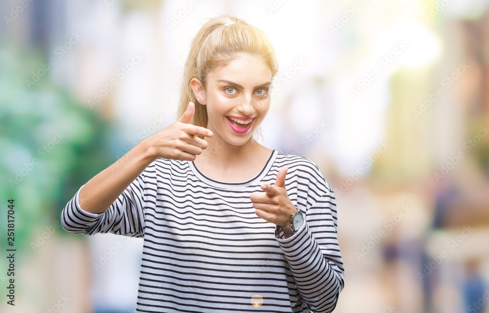 Young beautiful blonde woman wearing stripes sweater over isolated background pointing fingers to camera with happy and funny face. Good energy and vibes.