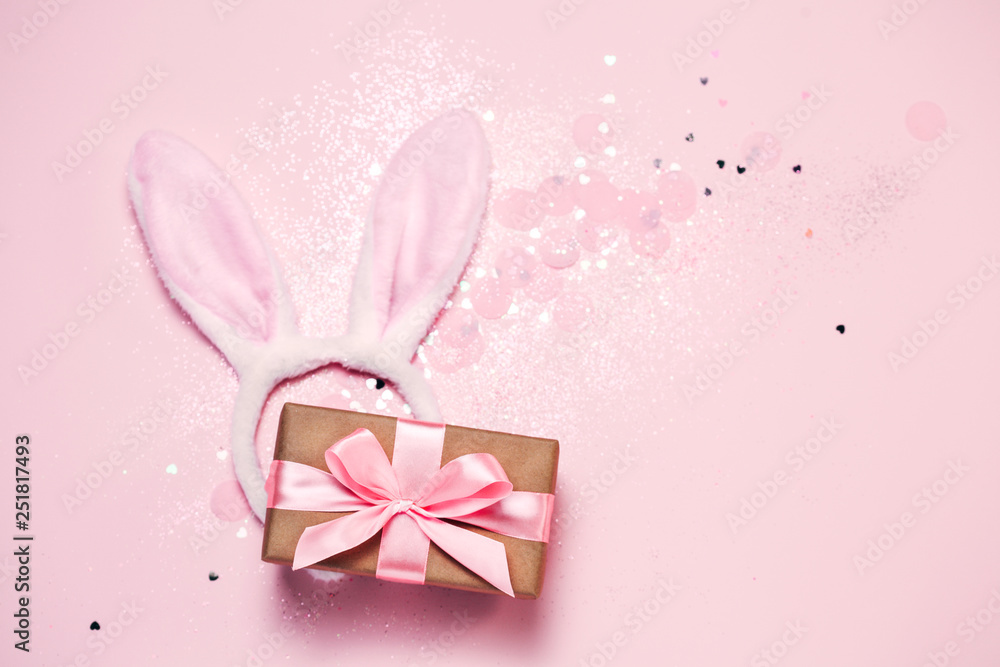 Top view and flat lay of Easter symbol - bunny ears and gift box on pink background. Festive and bright, confetti and sparks. Easter greetings Top view and flat lay of Easter symbol - bunny ears and gift box on pink background. Festive and bright, confetti and sparks. Easter greetings