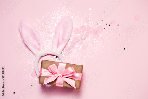 Top view and flat lay of Easter symbol - bunny ears and gift box on pink background. Festive and bright, confetti and sparks. Easter greetings