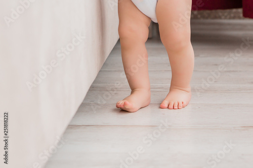 legs of a baby in a white bodysuit standing near the sofa