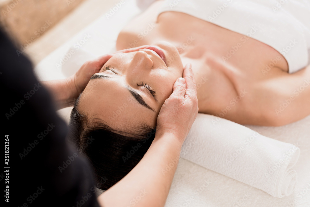 beautiful asian woman getting face massage with closed eyes at spa