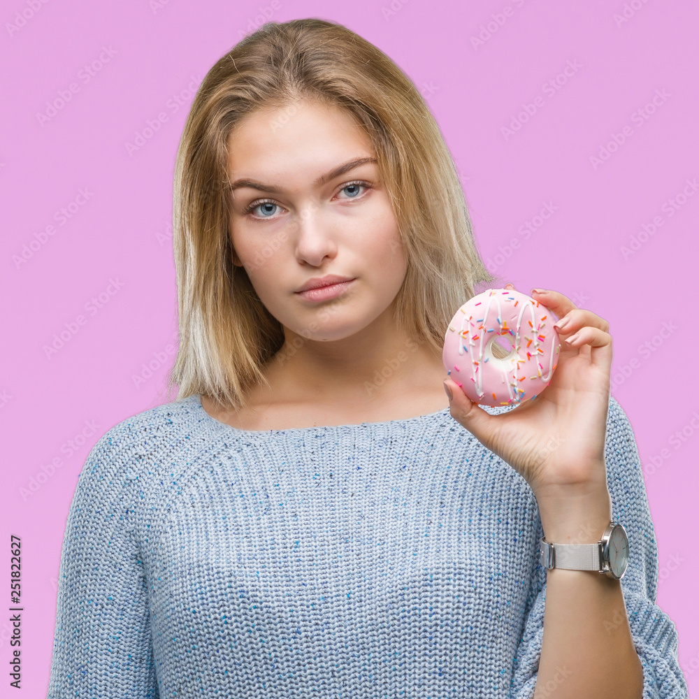 Young caucasian woman eating sweet donut over isolated background with a confident expression on smart face thinking serious Young caucasian woman eating sweet donut over isolated background with a confident expression on smart face thinking serious