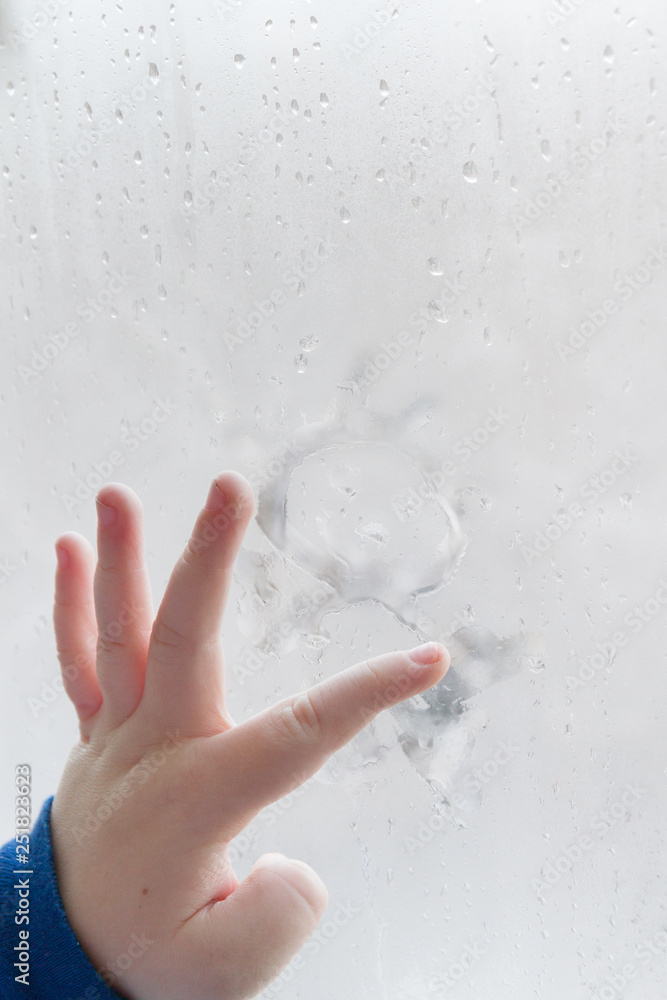 The child's hand draws a man on a frozen misted window in winter