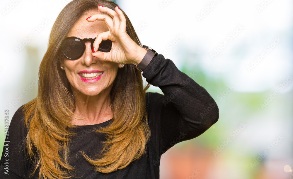 Naklejka premium Beautiful middle age woman wearing sunglasses doing ok gesture with hand smiling, eye looking through fingers with happy face.