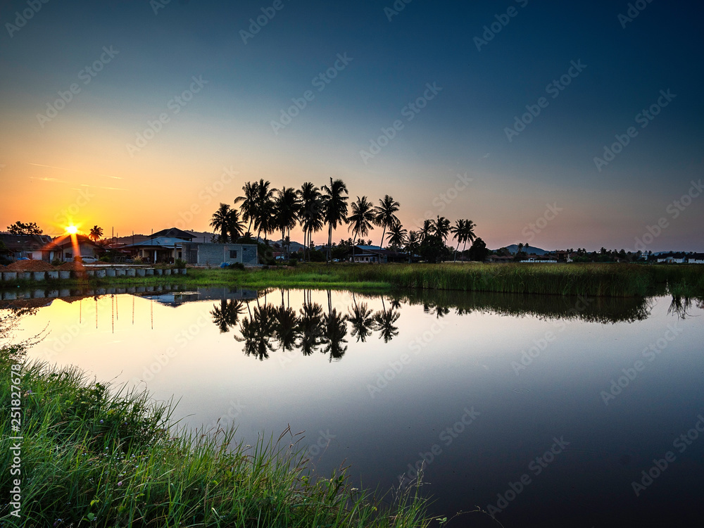 Obraz premium Reflection of palm and coconut trees on the water surface against beautiful sunrise background
