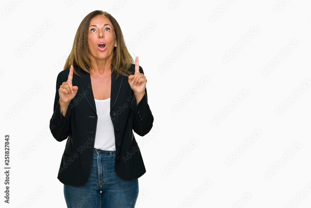 Beautiful middle age business adult woman over isolated background amazed and surprised looking up and pointing with fingers and raised arms.