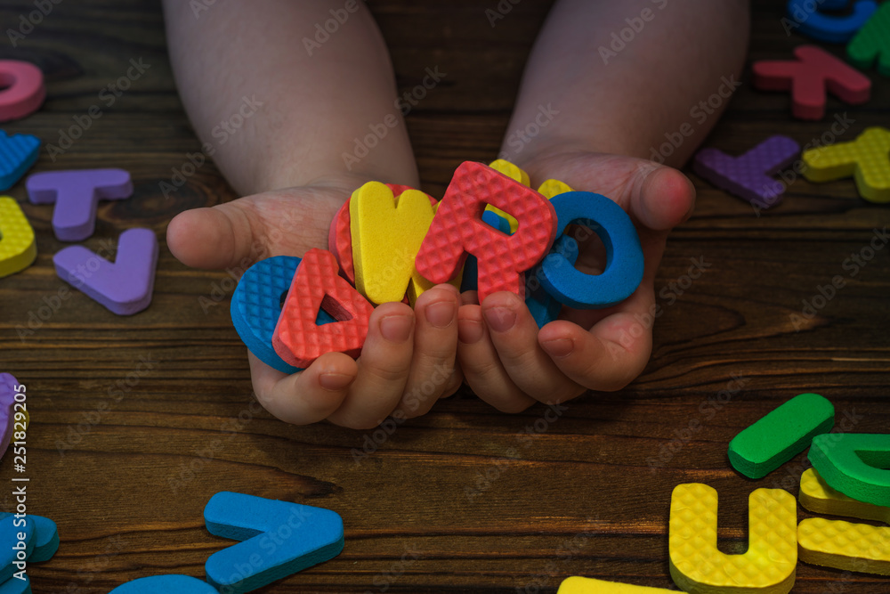 Letters in the hands of a child on the background of a wooden table. puzzle game, preschool education, alphabet.