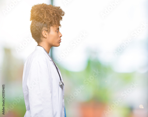 Young african american doctor woman over isolated background looking to side, relax profile pose with natural face with confident smile. © Krakenimages.com