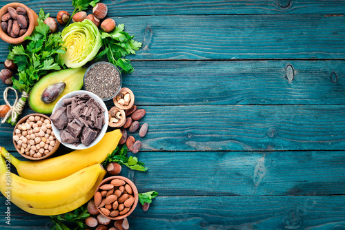 Foods containing natural magnesium. Mg: Chocolate, banana, cocoa, nuts, avocados, broccoli, almonds. Top view. On a blue wooden background.
