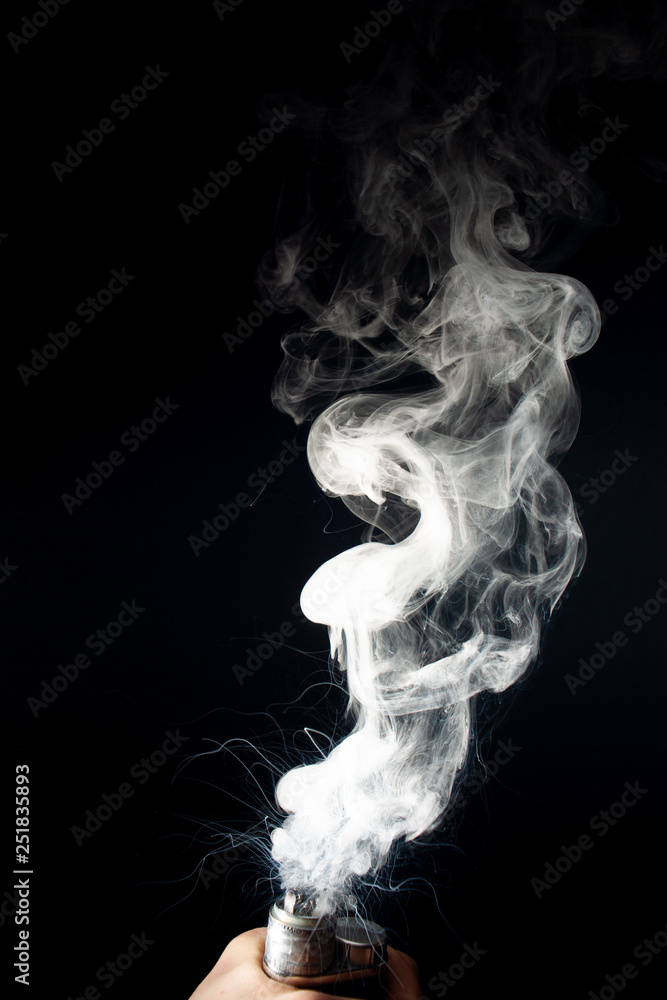 Male hand holds vape without atomiser. Column of vape clouds splash from coil on black background. Fog is white. Stock isolated white smoke with spray boiling glycerine. Male hand holds vape without atomiser. Column of vape clouds splash from coil on black background. Fog is white. Stock isolated white smoke with spray boiling glycerine.