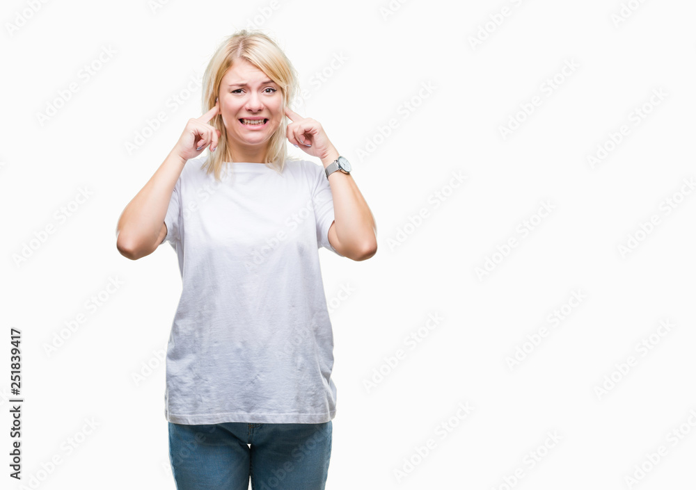 Young beautiful blonde woman wearing white t-shirt over isolated background covering ears with fingers with annoyed expression for the noise of loud music. Deaf concept. Young beautiful blonde woman wearing white t-shirt over isolated background covering ears with fingers with annoyed expression for the noise of loud music. Deaf concept.