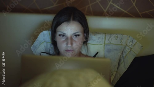 Woman lying on bed and working on laptor. girl working on a computer at night in bed. photo