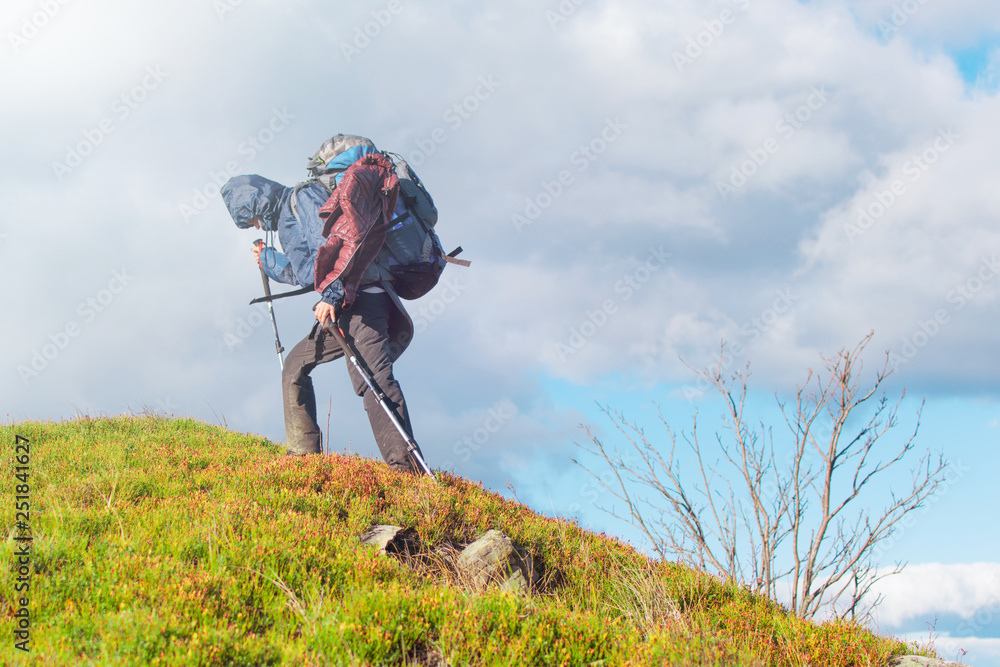 A woman with a backpack on a hike climbs the mountain.