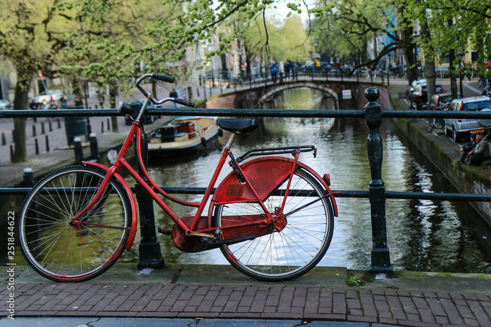 A picture of a lonely red bike on the bridge over the channel in Amsterdam.