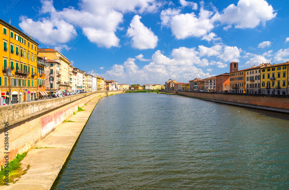 Row of old colorful buildings houses on embankment promenade of Arno river in historical centre of Pisa town with blue sky white clouds copy space background in sunny day, Tuscany, Italy