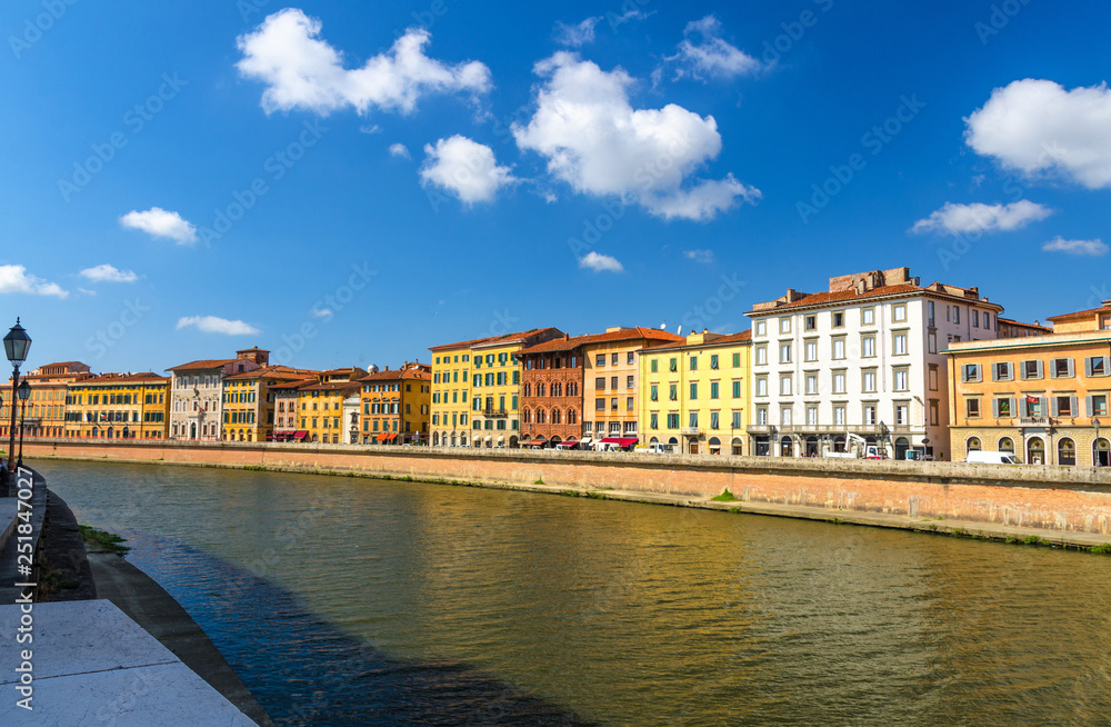 Row of old colorful buildings houses on embankment promenade of Arno river in historical centre of Pisa town with blue sky white clouds copy space background in sunny day, Tuscany, Italy