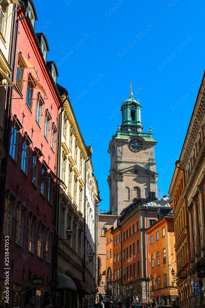 View onto Sankt Nikolai kyrka in Stockholm through a typical Swedish alley with colourful houses and cloud-free blue sky (Stockholm, Sweden, Europe)