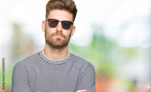 Young handsome man wearing sunglasses skeptic and nervous, disapproving expression on face with crossed arms. Negative person.