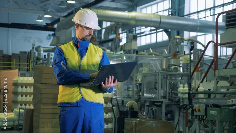 Person works with a laptop while standing in a factory room, modern technology. Person works with a laptop while standing in a factory room, modern technology.