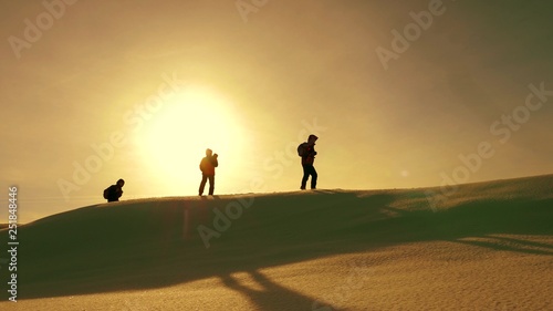 team of travelers follow each other along snow ridge against backdrop of yellow sunset. coordinated teamwork of tourists in winter. teamwork of people in difficult conditions.