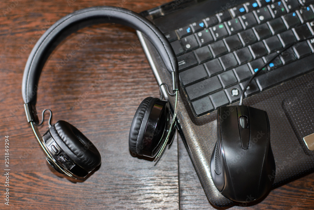 large black headphones lie on a wooden table next to a black laptop large black headphones lie on a wooden table next to a black laptop