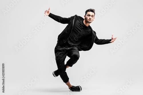 Dark-haired stylish young man wearing a black sweatshirt and black pants makes stylized movements of street dances