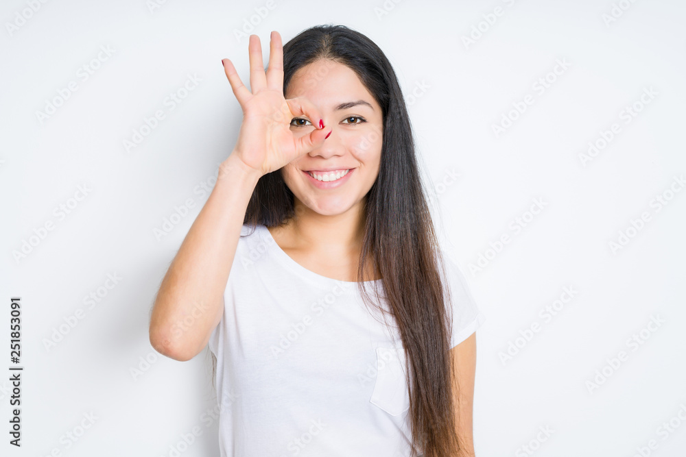 Beautiful brunette woman over isolated background doing ok gesture with hand smiling, eye looking through fingers with happy face. Beautiful brunette woman over isolated background doing ok gesture with hand smiling, eye looking through fingers with happy face.