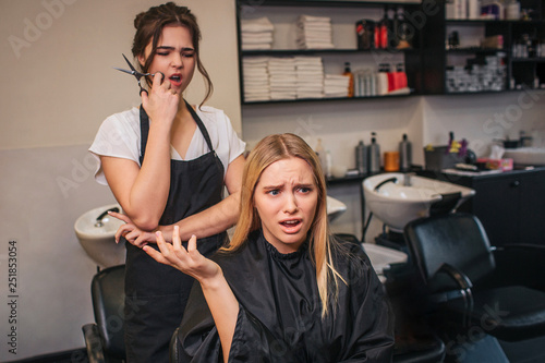 Angry blonde young female client screaming at hairdresser as a haircut done bad. Fight in beauty salon photo