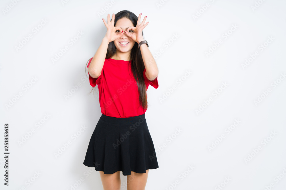 Beautiful brunette woman wearing red t-shirt and skirt over isolated background doing ok gesture like binoculars sticking tongue out, eyes looking through fingers. Crazy expression. Beautiful brunette woman wearing red t-shirt and skirt over isolated background doing ok gesture like binoculars sticking tongue out, eyes looking through fingers. Crazy expression.