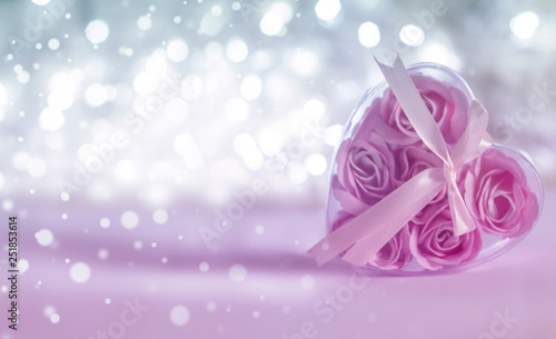 Box with pink roses inside in the form of a heart on a light background bokeh. Blurred white lights