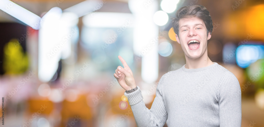 Young handsome man wearing winter sweater over isolated background with a big smile on face, pointing with hand and finger to the side looking at the camera.