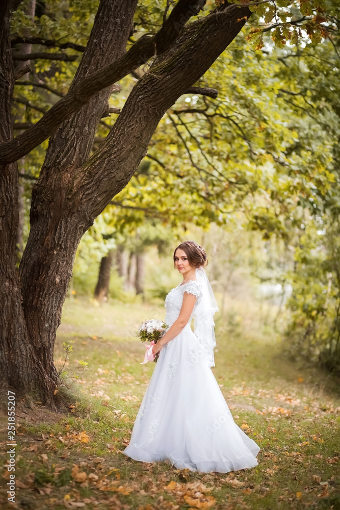 Bride with bridal bouquet. Attractive woman in the autumn park in white wedding dress