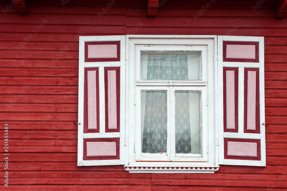 Red paint wooden rustic window in small cottage house. Vintage wall with transparent glass window and decorative red and white shutter.