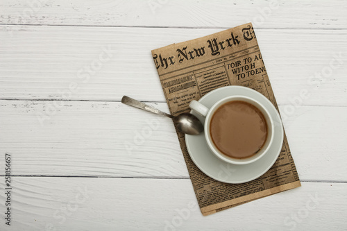 White cup with black coffee and old newspaper on a white woody background. Coffee on a white woody background. View from above. Place for text.