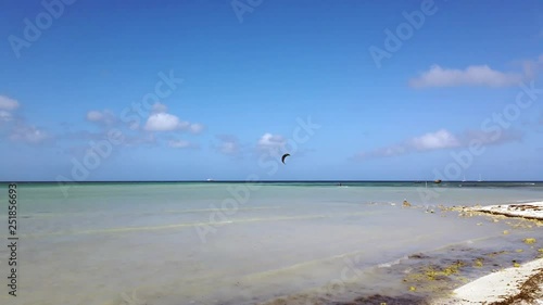 Beautiful blue green calm Caribbean Sea. The sky is blue with puffy clouds. There are kite surfers in the distance