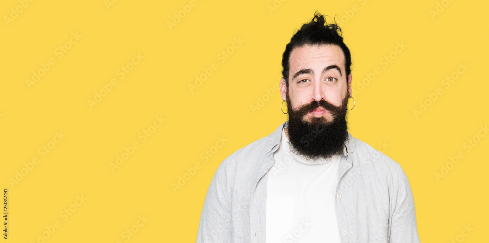 Fototapeta premium Young man with long hair, beard and earrings puffing cheeks with funny face. Mouth inflated with air, crazy expression.