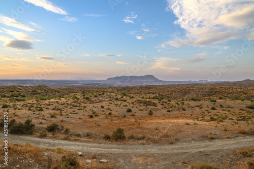 shape of a mountain at the horizon under a colorful sky with clouds in a desert