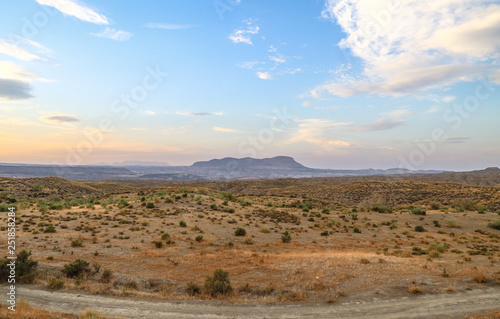 shape of a mountain at the horizon under a colorful sky with clouds in a desert