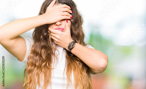 Young beautiful woman wearing casual white t-shirt Covering eyes and mouth with hands, surprised and shocked. Hiding emotion