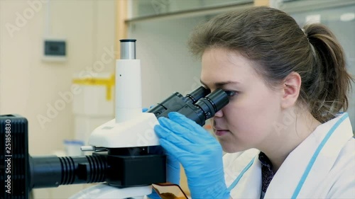 Young female scientist watches through the mircoscopical objective in the chemical laboratory and smiles photo