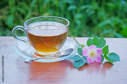 Glass cup with tea and wild rose flower on a background of grass