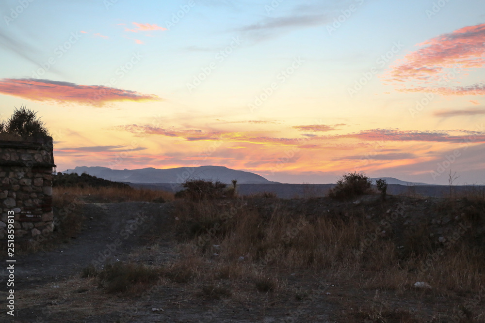 sunset over the mountains in a steppe region with dry grass and colorful sky