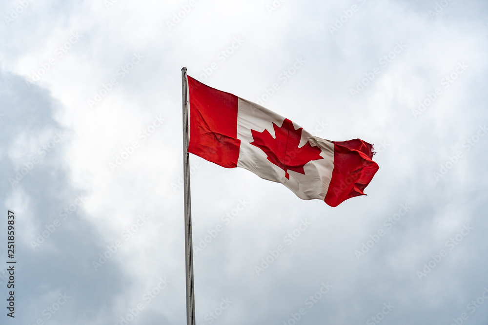 Flag of Canada (or in French Le drapeau du Canada) fluttering against cloudy sky Flag of Canada (or in French Le drapeau du Canada) fluttering against cloudy sky