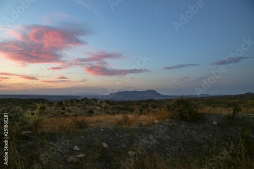 sunset over a mountain with purple red clouds and a blue sky at a grassland landscape