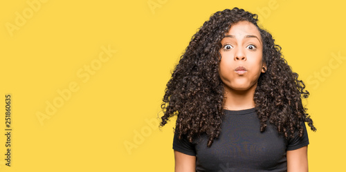 Quadro su tela Young beautiful woman with curly hair puffing cheeks with funny face