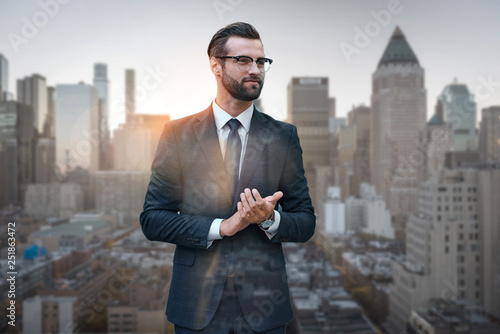 Satisfied with work done. Excited young businessman in suit rubbing his hands and looking away while standing against of morning cityscape background